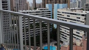 A high-rise building with multiple floors, a pool area, and a view of other buildings in the background. - In this cozy condominium located in Waikiki (Honolulu)
