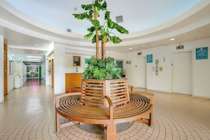 A lobby with a wooden bench and a central planter with tropical plants. - In this cozy condominium located in Waikiki (Honolulu)