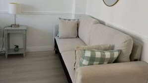 A minimalist living room with a beige sofa, a small side table with a lamp, and a round mirror on the wall. - In this cozy condominium located in Waikiki (Honolulu)