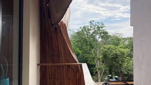 Un edificio moderno con un design originale caratterizzato da un tetto spiovente in legno, un balcone in cemento e vista su alberi e cielo nuvoloso.