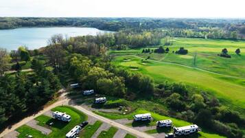 An aerial view of a campground with RVs parked in designated areas, surrounded by lush greenery and a golf course.