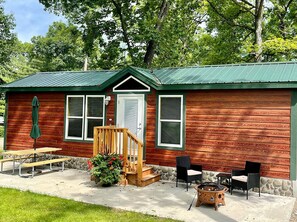 A rustic cabin with a green metal roof, wooden exterior, and a front porch with a bench and chairs. - Yellowstone Chalet Cottage (Hartland Township)