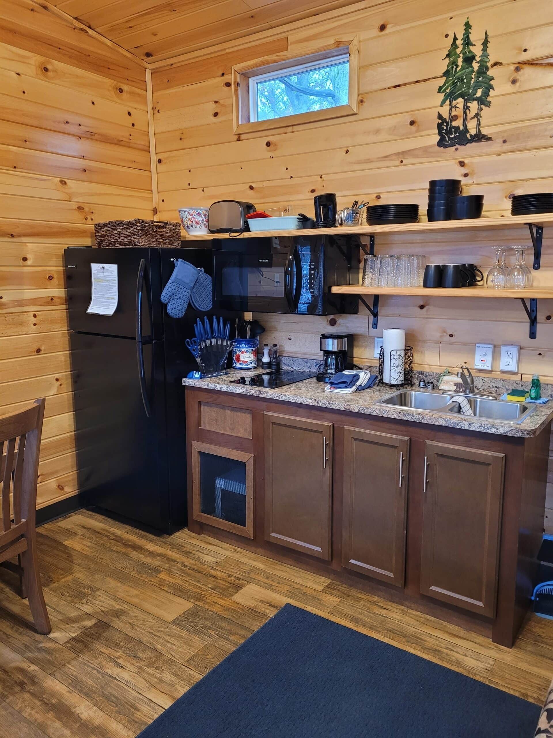 Una cocina compacta con paredes de madera, un refrigerador integrado, un microondas y un lavamanos.