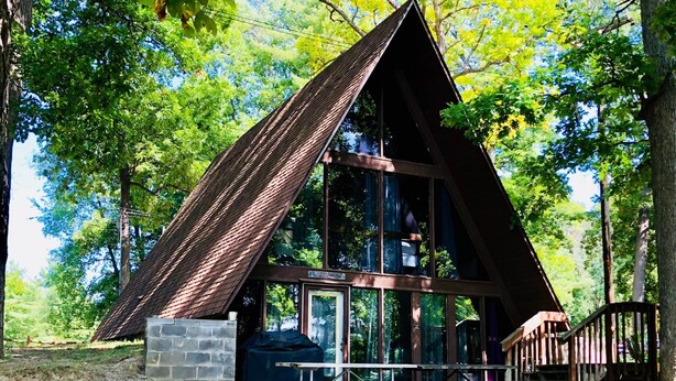 A wooden cabin with a sloped roof, large windows, and a stone foundation. - A-Frame Historic Cottage (Hartland Township)