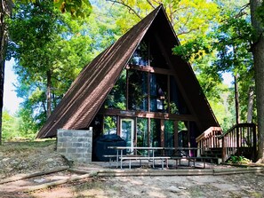 A wooden cabin with a sloped roof, large windows, and a stone foundation. - A-Frame Historic Cottage (Hartland Township)