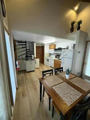 A compact kitchen with white cabinets, a microwave, and a refrigerator. There is a dining table with four chairs and a decorative centerpiece.
