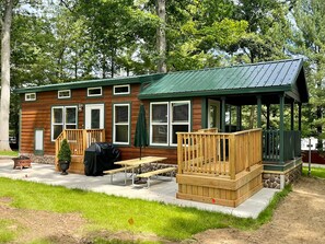 A wooden cabin with a covered porch, picnic tables, and a barbecue grill. - Glacier Chalet Cottage (Hartland Township)