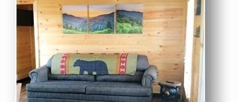 A cozy cabin interior with a sofa, a rug, and two framed landscape paintings on the wall.