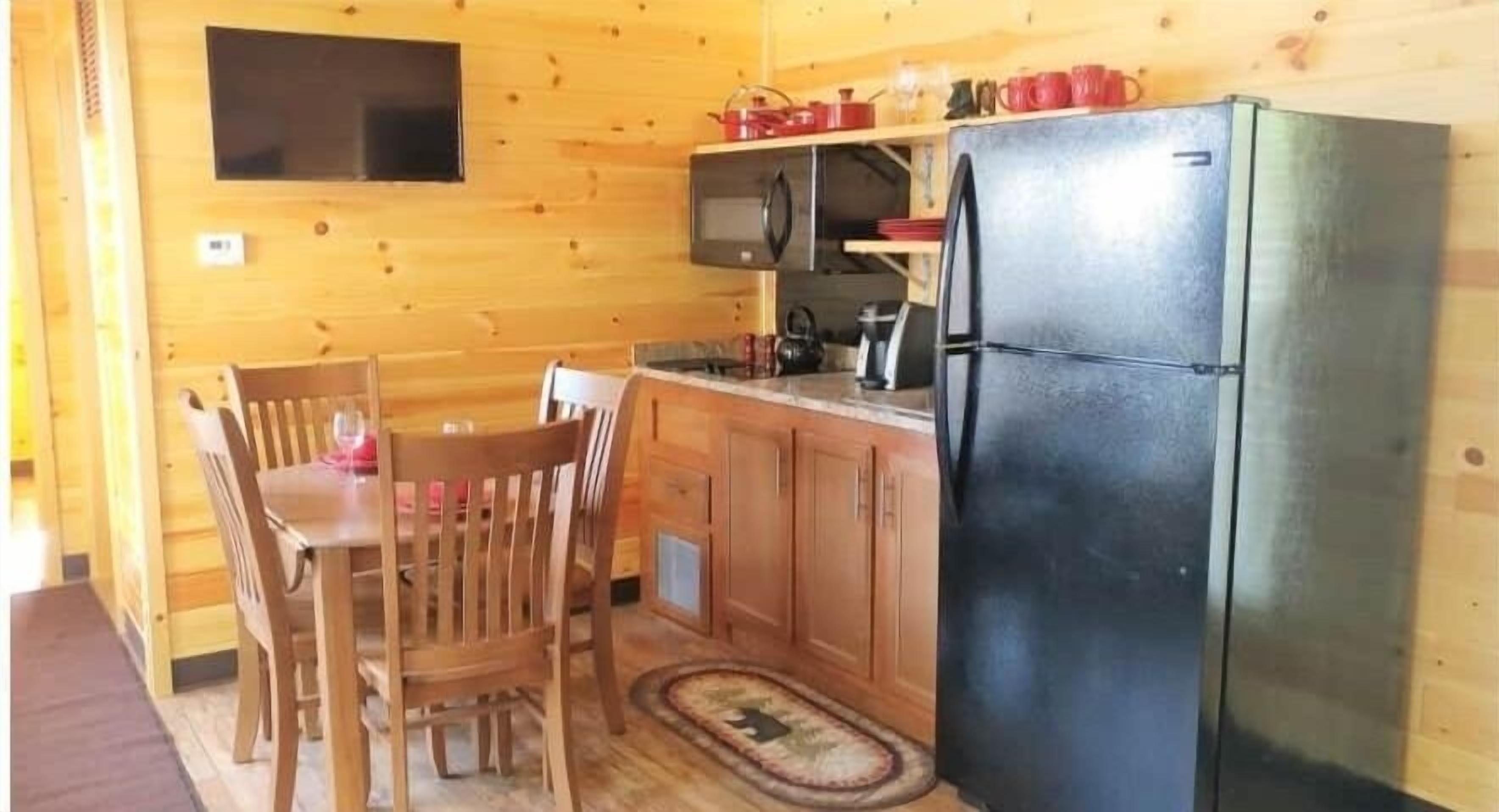 Eine kleine Küche mit Holzschränken, einem schwarzen Kühlschrank und einem Essbereich mit Holztisch und Stühlen.