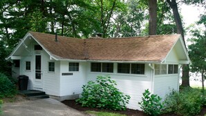 A small, single-story cabin with a sloped roof, a front porch, and a small front yard with a pathway leading to the entrance.