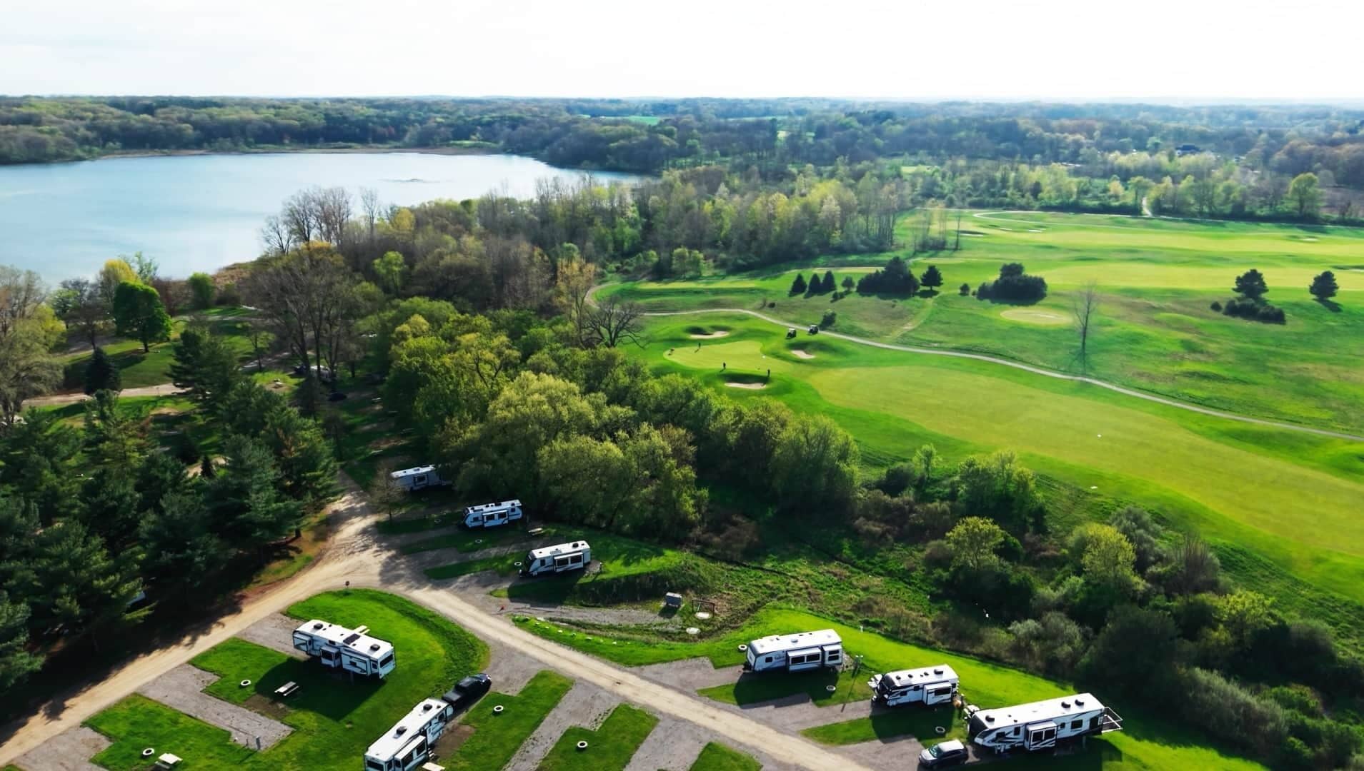 Vista aérea de un camping con vehículos recreativos estacionados en zonas delimitadas, rodeado de exuberante vegetación y un campo de golf.