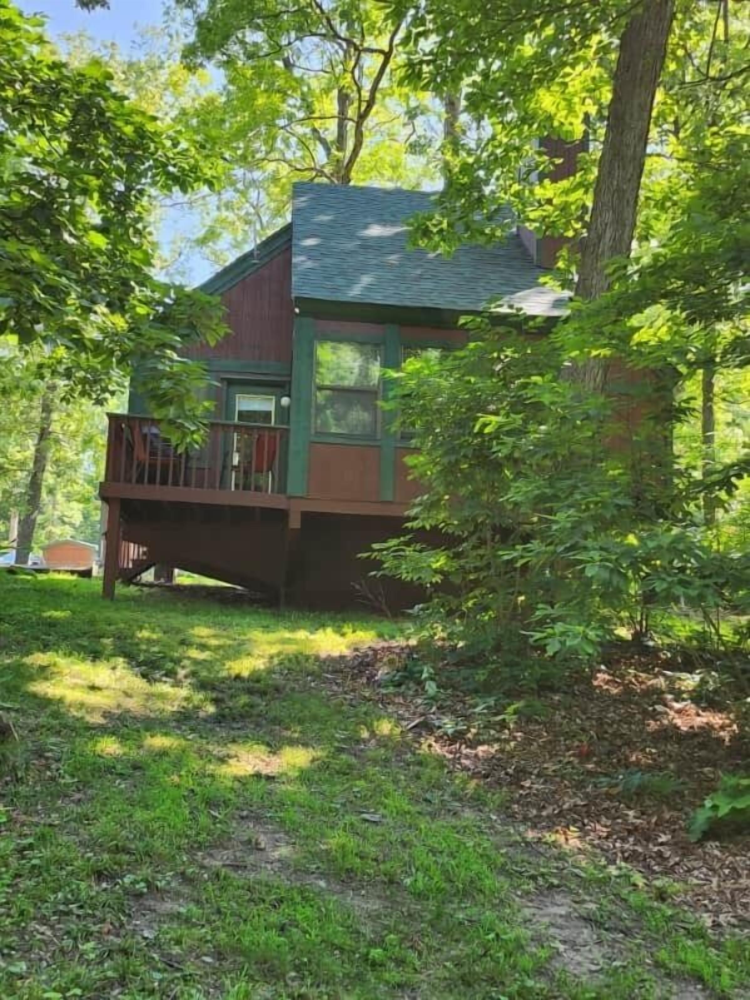 A cabin with a balcony, surrounded by trees and a grassy area.