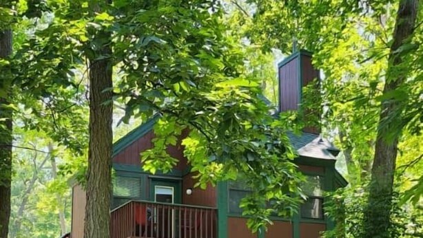 A cabin with a wooden deck, surrounded by trees.