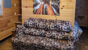 A cozy cabin interior with a wooden ceiling, a large window, and a sofa with animal prints. - Redwood Chalet Cottage (Hartland Township)