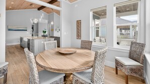 A modern kitchen with white cabinets, a central island, and a dining area with wicker chairs and a wooden table. - Coastal Sunsets - Vacation Rental in 30A with Private Pool (Santa Rosa Beach)