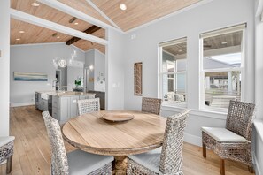 A modern kitchen with white cabinets, a central island, and a dining area with wicker chairs and a wooden table. - Coastal Sunsets - Vacation Rental in 30A with Private Pool (Santa Rosa Beach)