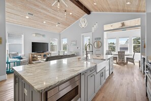A spacious kitchen with a large island, wooden flooring, and a high ceiling with exposed beams. - Coastal Sunsets - Vacation Rental in 30A with Private Pool (Santa Rosa Beach)