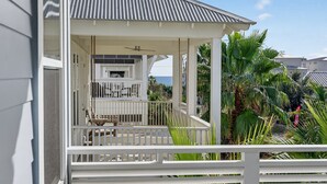 A covered outdoor area with a ceiling fan, a table, and chairs, surrounded by palm trees and a view of the ocean. - Coastal Sunsets - Vacation Rental in 30A with Private Pool (Santa Rosa Beach)