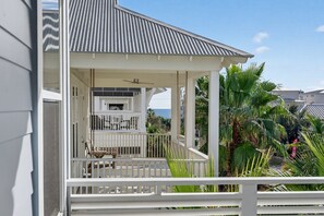 A covered outdoor area with a ceiling fan, a table, and chairs, surrounded by palm trees and a view of the ocean. - Coastal Sunsets - Vacation Rental in 30A with Private Pool (Santa Rosa Beach)