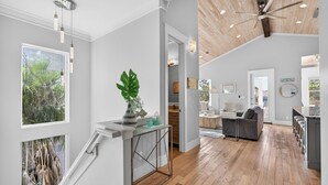 A spacious living area with a wooden floor, a dining area, and a kitchen. There is a staircase with a view of greenery outside. - Coastal Sunsets - Vacation Rental in 30A with Private Pool (Santa Rosa Beach)