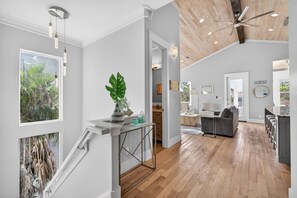 A spacious living area with a wooden floor, a dining area, and a kitchen. There is a staircase with a view of greenery outside. - Coastal Sunsets - Vacation Rental in 30A with Private Pool (Santa Rosa Beach)