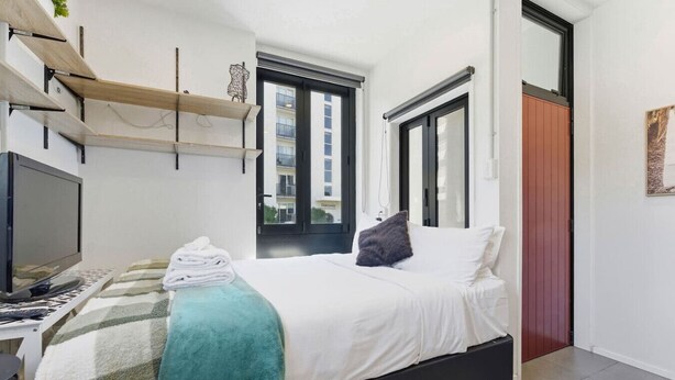 Un dormitorio con una cama, televisión, ventana y puerta.