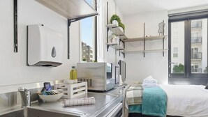 Una habitación de hotel moderna con un lavamanos grande, una cama con una manta color turquesa, un televisor de pantalla plana y un ventanal con vistas a la ciudad.