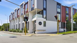 Un edificio moderno de varios pisos con paneles exteriores en blanco y rojo, ventanas grandes y una entrada visible.