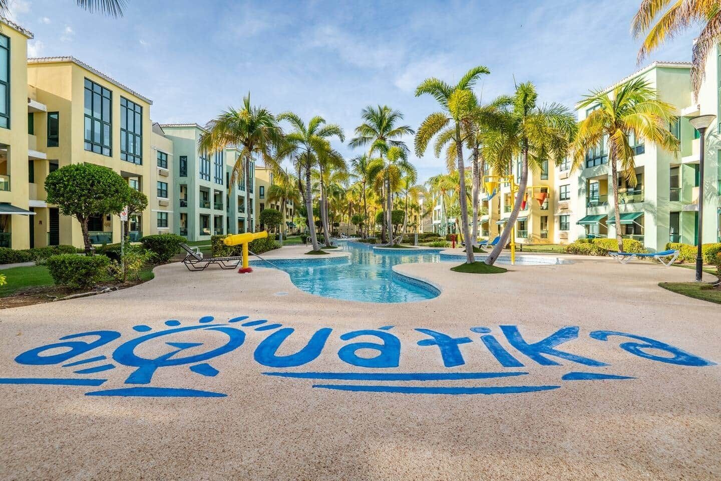 Un resort con piscina, palmeras y un edificio con un letrero azul que dice "aquatiko".
