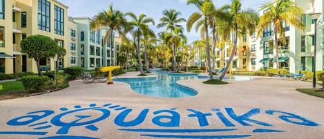 Un resort con piscina, palmeras y un edificio con un letrero azul que dice "aquatiko".