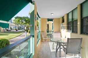 A balcony with a glass table and chairs, a view of the courtyard, and a building with a green awning. - The Best Apartment in Aquatika (Vieques)