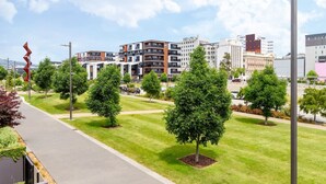 A modern urban area with a well-maintained grassy area, several trees, and contemporary buildings in the background. - 2-Bedroom w/ Carpark. Overlooks Central East Frame (Christchurch)