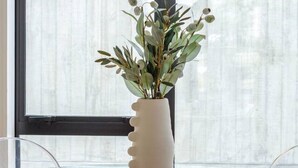 A dining table with a glass top and wooden base, surrounded by clear chairs. A white vase with green foliage is placed on the table. - 2-Bedroom w/ Carpark. Overlooks Central East Frame (Christchurch)