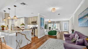 A modern kitchen with a marble island, pendant lighting, and wooden flooring.