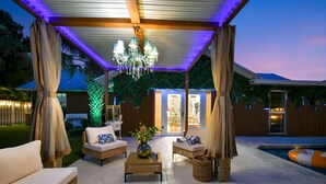 An outdoor patio area with wicker furniture, a chandelier, and a pool.