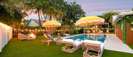 A backyard with a swimming pool, lounge chairs, and umbrellas.