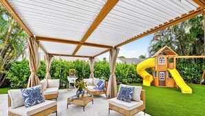 A covered patio with wicker furniture and a playhouse with a slide.