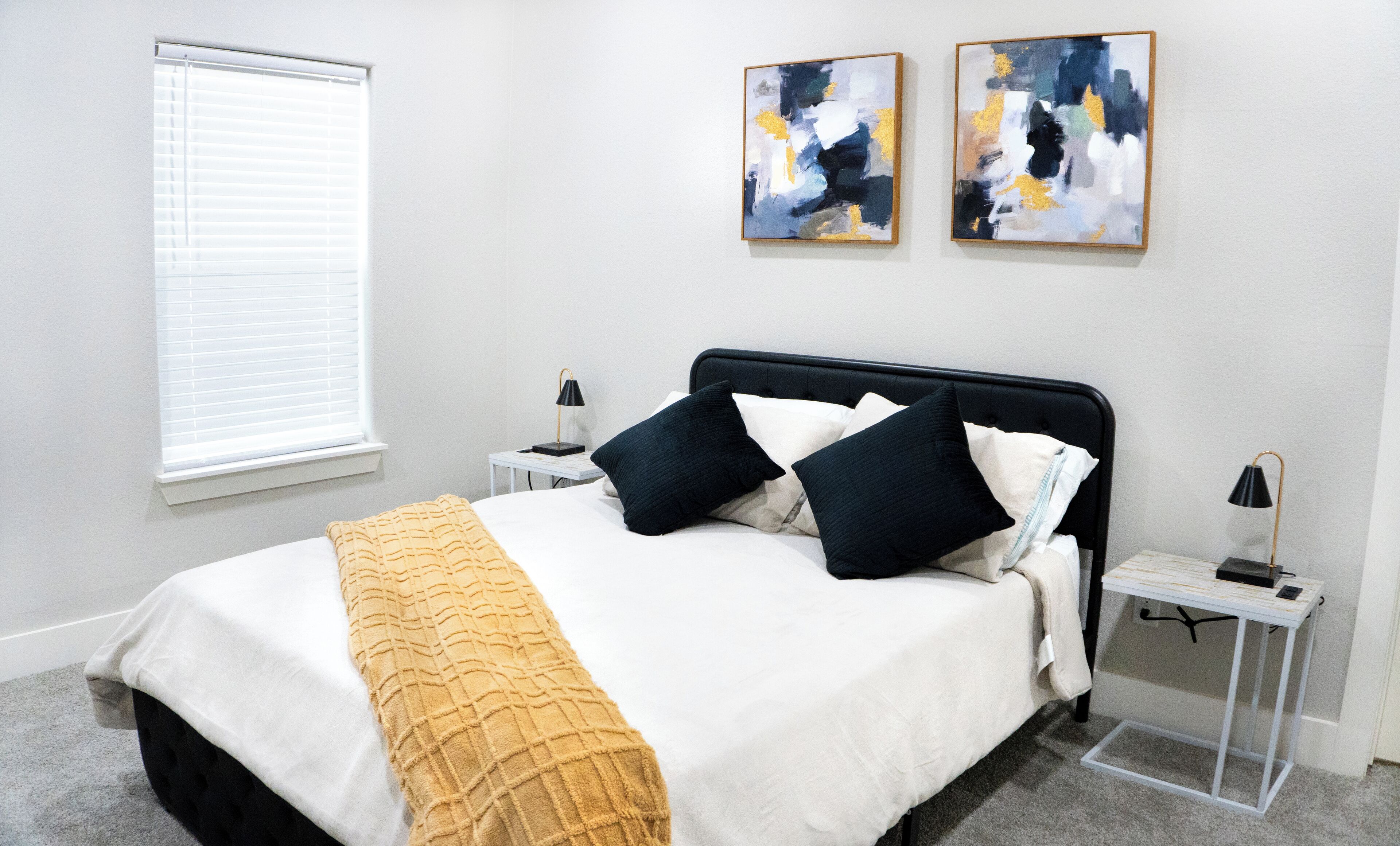 Ein ordentlich eingerichtetes Schlafzimmer mit einem Bett, Nachttischen und Kunstwerken an der Wand.