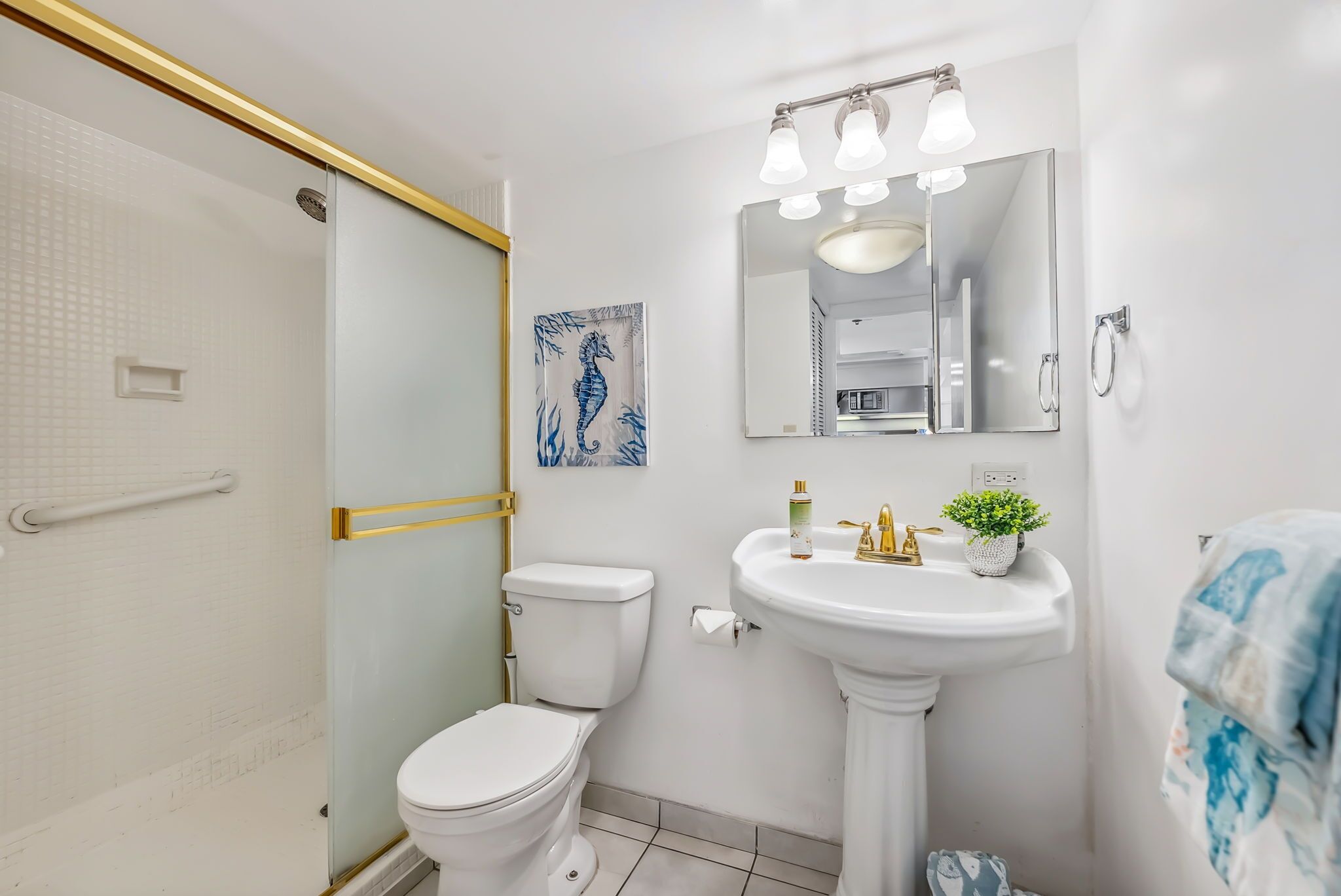 A bathroom with a glass shower enclosure, a white toilet, a pedestal sink with a mirror above it, and a small potted plant on the sink.