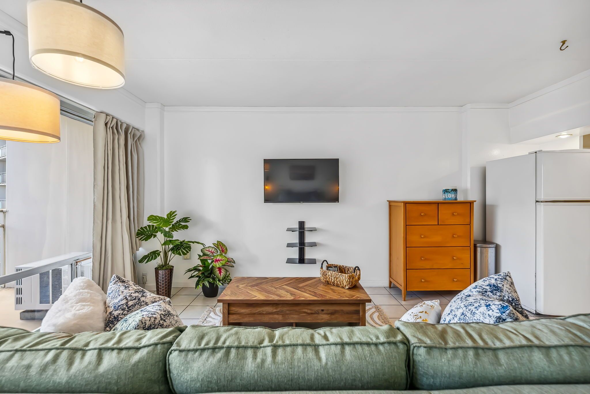 Un salon moderne comprenant un canapé, une table basse en bois, une plante en pot, un meuble en bois et un téléviseur fixé au mur.