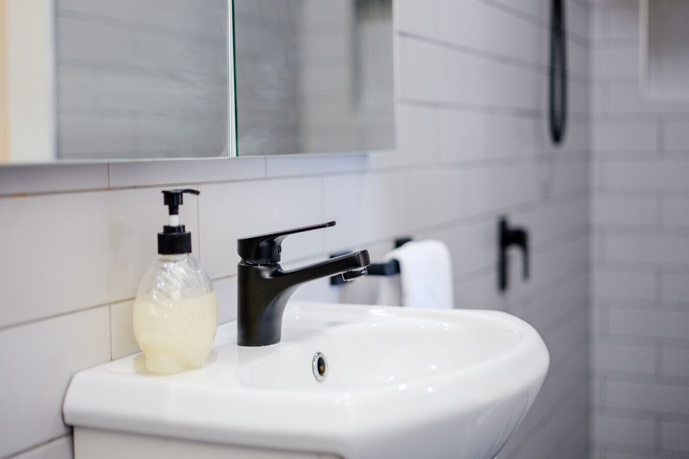 Ein weißes Waschbecken mit einem schwarzen Wasserhahn und einer transparenten Seifenspenderflasche.
