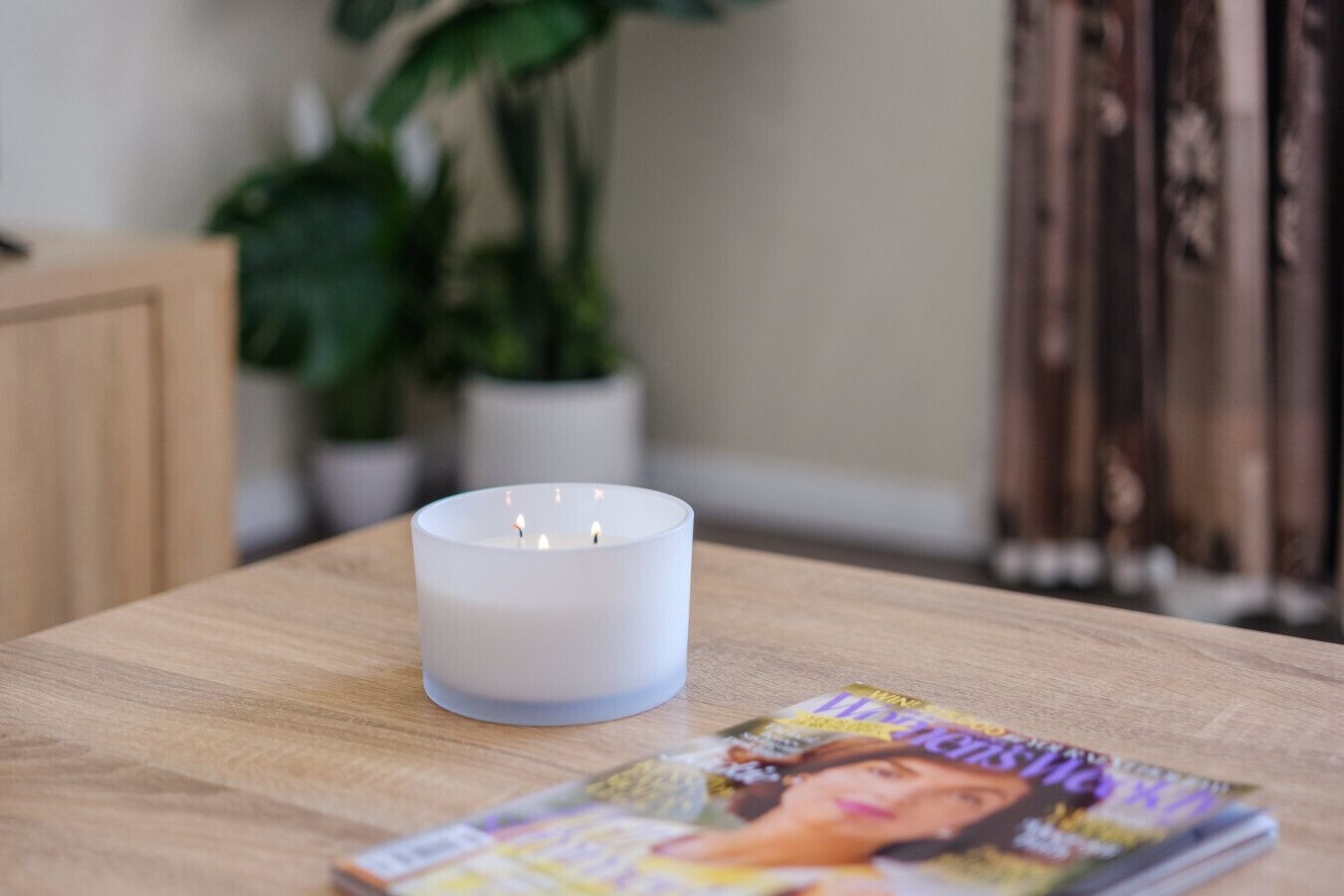 Een witte kaars op een houten tafel, voor zich een tijdschrift.