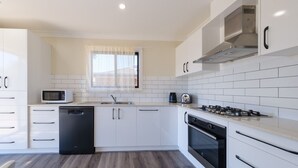 A modern kitchen with white cabinetry, a microwave, a sink, a stove, and a dishwasher.
