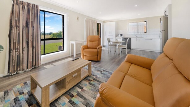 A modern living room with a sofa, a chair, a coffee table, and a view of a green landscape through a large window.
