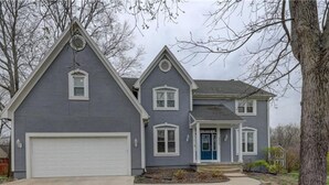 A two-story house with a garage, a front porch, and a well-maintained lawn. - Welcome World Cup fans to this Spacious 5-bedroom house with Modern updates (Overland Park)