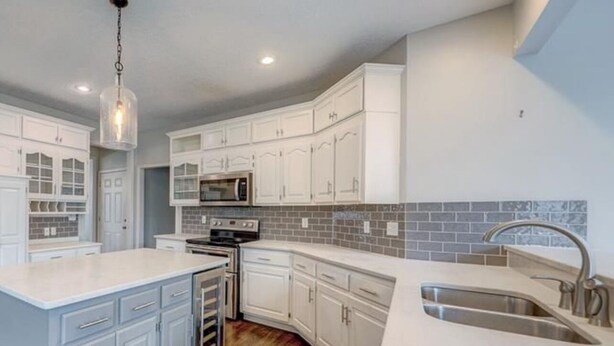 A modern kitchen with white cabinetry, a central island, a built-in oven, and a stainless steel sink. - Welcome World Cup fans to this Spacious 5-bedroom house with Modern updates (Overland Park)