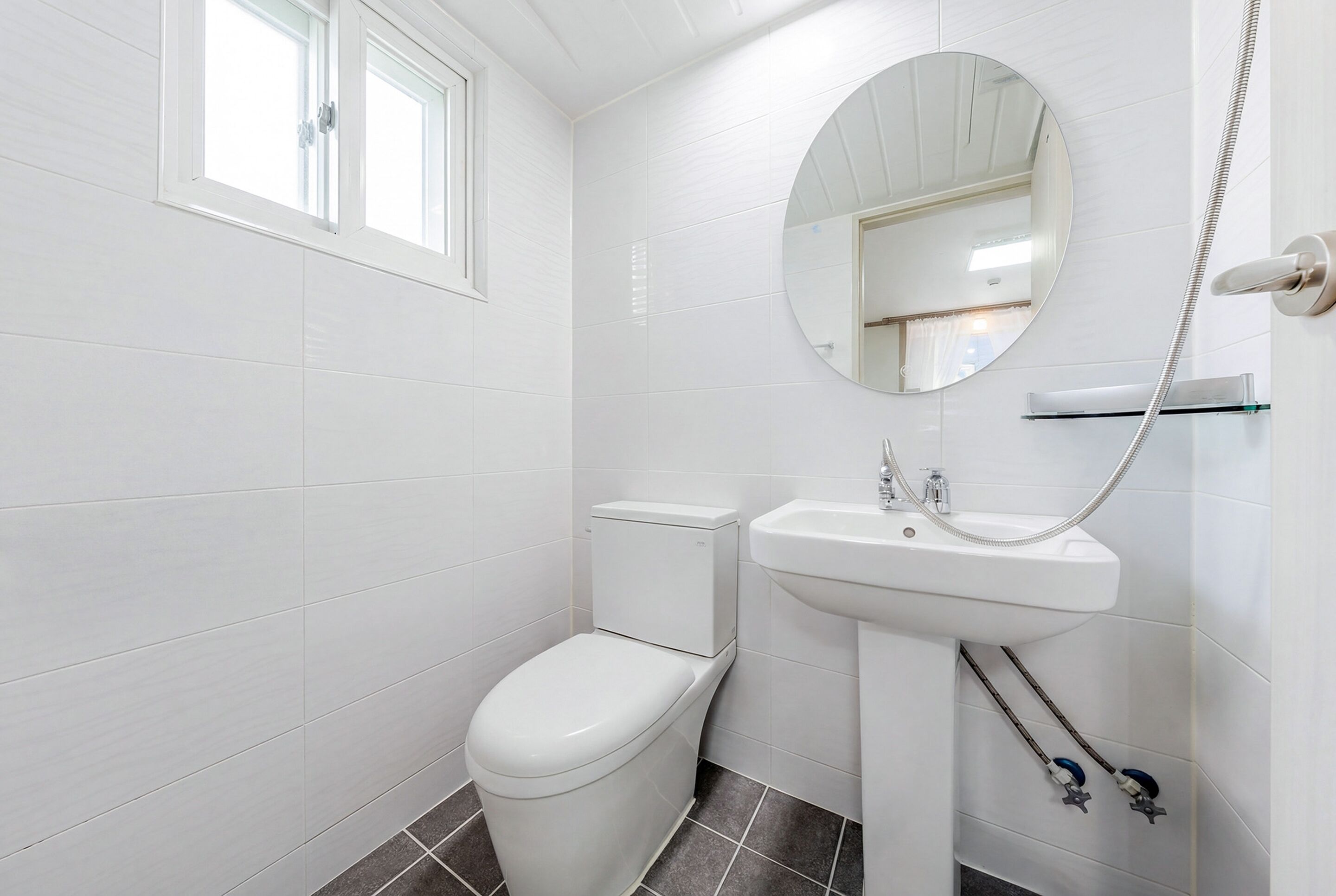 A modern bathroom with a toilet, sink, and a round mirror.