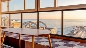 Une pièce dotée d’une grande fenêtre donnant sur la mer, d’une table en bois et d’un tapis à motifs.