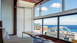 Une chambre moderne dotée d’une grande fenêtre, d’un canapé, d’une petite table et offrant une vue sur la mer et les bâtiments.