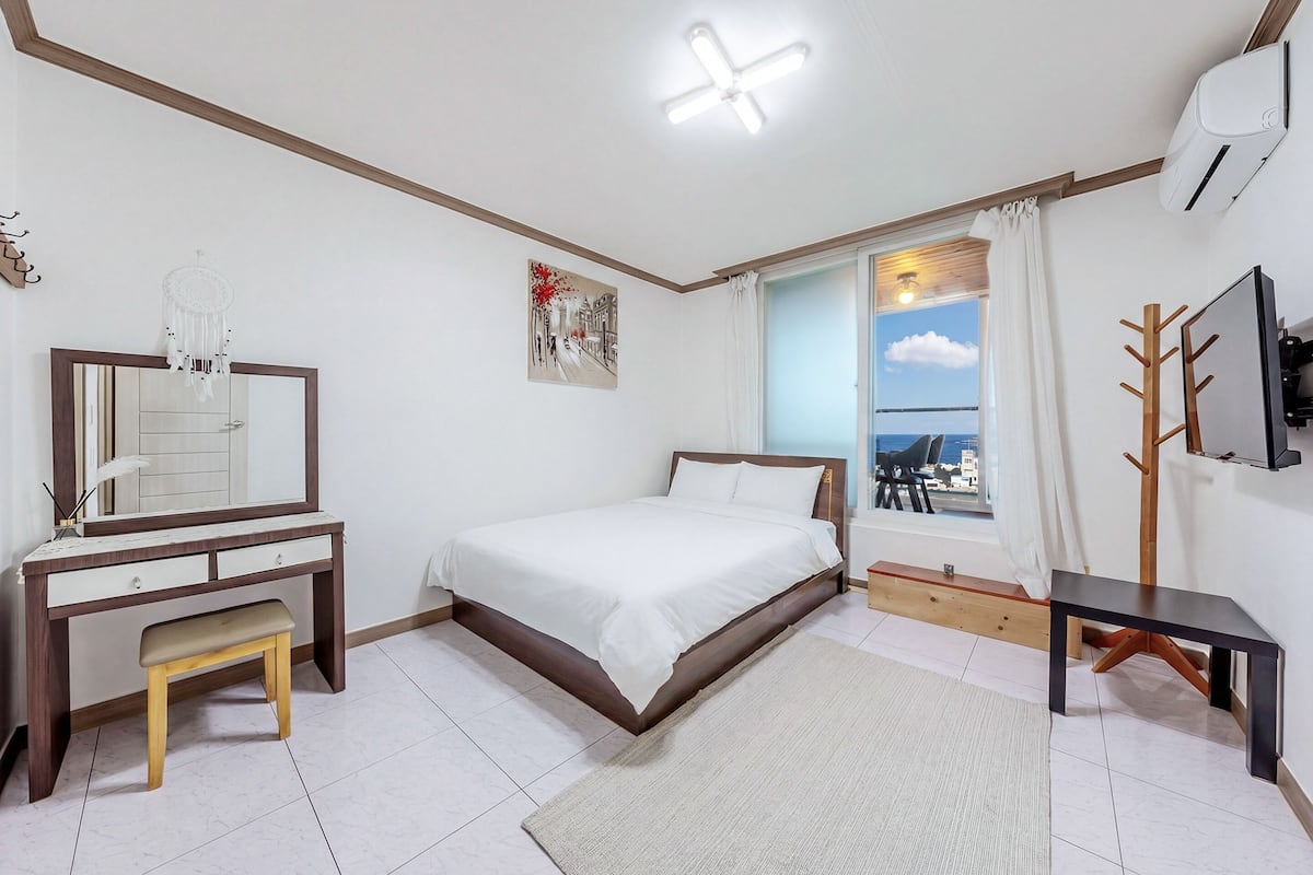 Une chambre à coucher avec un lit, un bureau avec une chaise, une télévision et une fenêtre avec des rideaux.